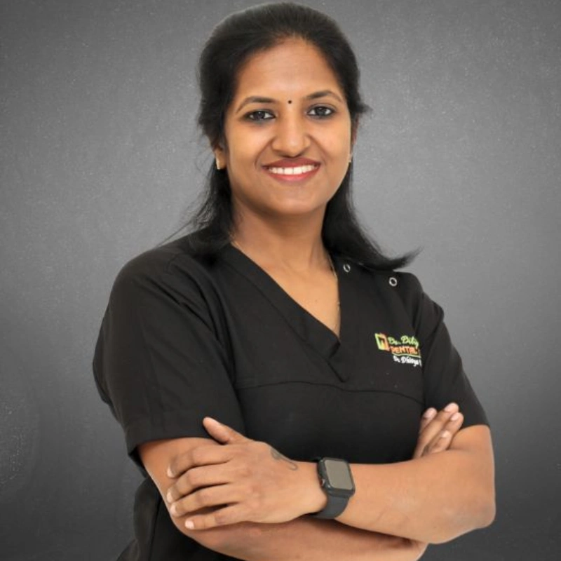 A professional portrait of Dr. Dhivya Dilipkumar, recognized as the best dentist in Chennai, smiling in her black clinical uniform with arms crossed at Dr. Dilip Dental Centre.