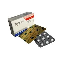 A high-angle shot looking down at a box of Amdocal-5 tablets next to two overlapping blister strips, showing both the gold-colored foil backing and the clear bubble side containing the pills.