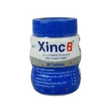 A small plastic supplement bottle of Xinc B tablets featuring a white and blue label with a solid blue plastic screw cap.